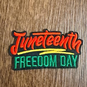 Puede incluir: Parche bordado del Día de la Libertad del Juneteenth. El texto en rojo, amarillo y verde sobre un fondo negro. La palabra "Juneteenth" está en una fuente de escritura sobre "Freedom Day".
