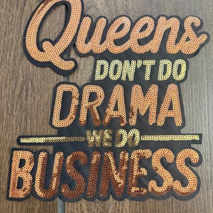 May include: A black fabric patch featuring the text Queens DON'T DO DRAMA WE DO BUSINESS in shimmering copper and gold sequins. The word Queens is at the top, followed by DON'T DO DRAMA, a horizontal line, WE DO, and BUSINESS at the bottom.