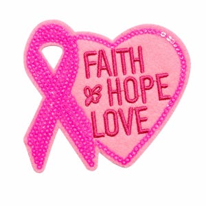 May include: A pink heart-shaped patch featuring a sequined awareness ribbon on the left side. The patch is made of felt and includes the embroidered text FAITH HOPE LOVE in dark pink thread, with a small butterfly icon next to the word FAITH.