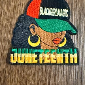 May include: Embroidered patch featuring a Black woman wearing a cap with the text "BLACKGIRLMAGIC." The patch also includes the word "JUNETEENTH" in green and yellow. The woman has gold hoop earrings and red lipstick.