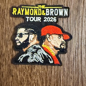 Könnte beinhalten: Gestickter Aufnäher mit zwei Männerprofilen, einer mit Sonnenbrille, der andere mit roter Kappe. Der Aufnäher trägt die Aufschrift "THE RAYMOND & BROWN TOUR 2026" in gelben und weißen Buchstaben auf schwarzem Hintergrund.