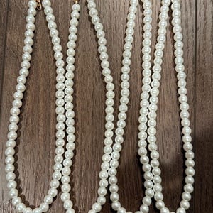 May include: Four necklaces featuring uniform white spherical beads arranged in a single strand. Each necklace is finished with a gold-toned metal lobster claw clasp and an adjustable extender chain at the end to allow for a customized fit.