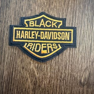 May include: Black Harley-Davidson Riders patch with yellow embroidered text and border. The patch features the Harley-Davidson logo shape, with the words "BLACK", "HARLEY-DAVIDSON", and "RIDERS" in a bold, readable font.