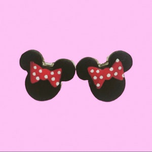 May include: A pair of black mouse-shaped earrings with red bows and white polka dots. The earrings are set against a light pink background.