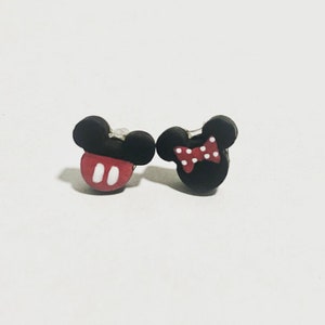 May include: A pair of black and red Mickey Mouse and Minnie Mouse stud earrings. The Mickey Mouse earring has a red base with white oval details. The Minnie Mouse earring has a red and white polka dot bow.