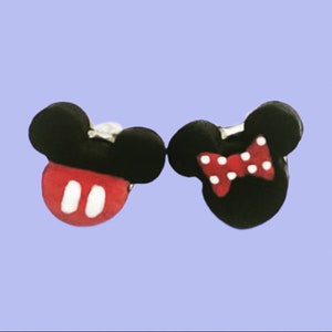 May include: A pair of black and red Mickey and Minnie Mouse-themed earrings. One earring has a red face with white accents and black ears. The other earring features a red bow with white polka dots and black ears.