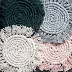 Puede incluir: Cuatro posavasos de ganchillo hechos a mano con flecos. Los posavasos son en tonos de verde, gris, blanco y rosa.