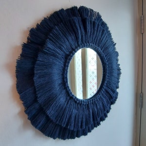 Puede incluir: Un espejo redondo con un borde de flecos azul marino. El espejo est&aacute; rodeado por m&uacute;ltiples capas de flecos, creando un aspecto texturizado y decorativo.