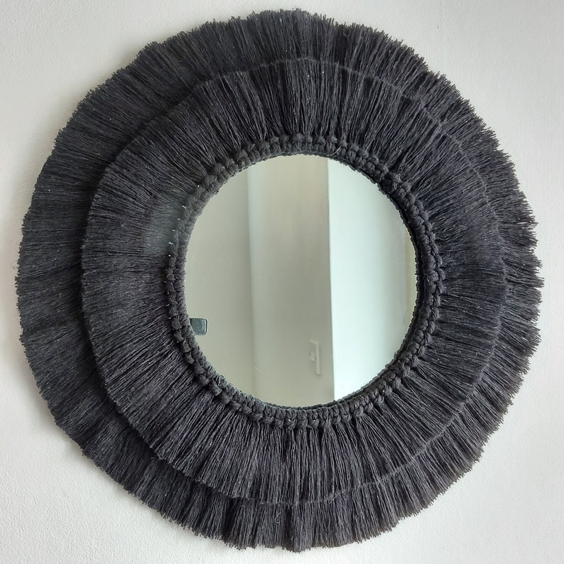 Puede incluir: Un espejo redondo con un borde de flecos negros. El espejo tiene un dise&ntilde;o simple y moderno y a&ntilde;adir&iacute;a un toque de estilo bohemio a cualquier habitaci&oacute;n.