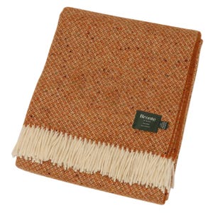 May include: An orange and tan woven wool throw blanket with a cream fringe. The blanket has a textured appearance and a small green tag that reads "Bronte by Moon". The blanket is folded neatly.