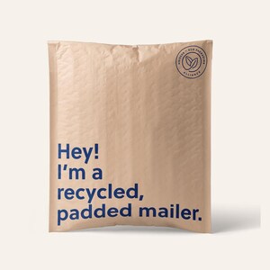 May include: A light tan, rectangular padded mailer with a textured surface. The front features dark blue text that reads, "Hey! I'm a recycled, padded mailer." A circular logo in the top right corner contains the text "noissue. eco packaging alliance."