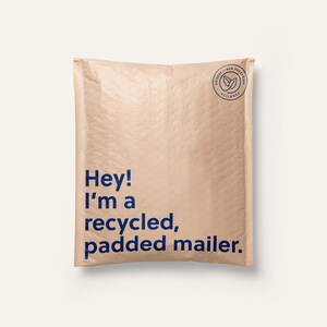May include: A light tan, rectangular padded mailer with a textured surface. The front features dark blue text that reads, "Hey! I'm a recycled, padded mailer." In the top right corner, there is a circular logo with the text "noissue eco packaging alliance."