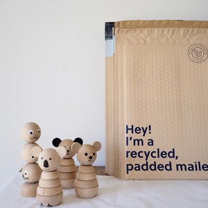 May include: Four wooden animal figurines with smooth, light-coloured surfaces and painted facial features, standing next to a stack of tan, bubble-padded mailers with the printed text: Hey! I'm a recycled, padded mailer.