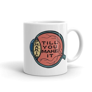 May include: White ceramic coffee mug featuring a colourful illustration of an eye with the text "Till You Make It" inside the eye.