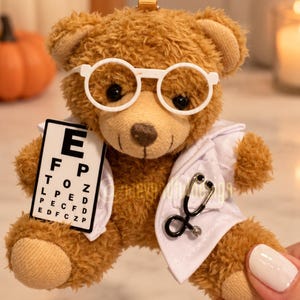 Könnte beinhalten: Ein brauner Plüschteddybär mit einer weißen Kunststoffbrille und einem weißen Arztkittel. Der Bär hält eine kleine weiße Sehtafel mit schwarzen Buchstaben in einer Pfote und trägt ein schwarz-silbernes Stethoskop am Kittel.
