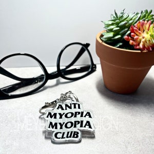 May include: A clear acrylic keychain with the text "ANTI MYOPIA MYOPIA CLUB" in black lettering.
