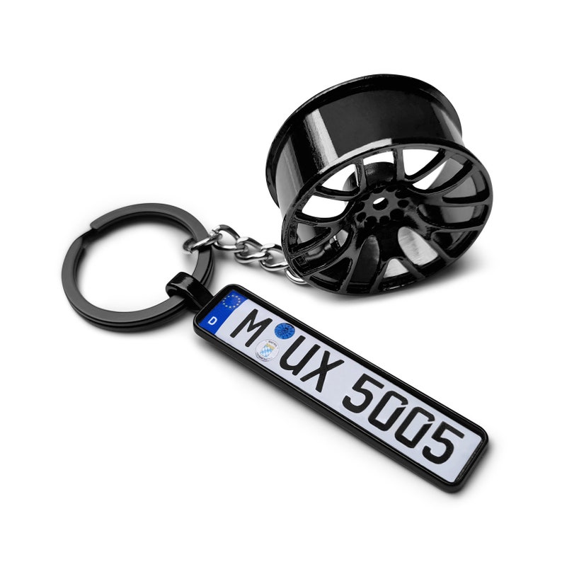 May include: Black metal car wheel keychain with a black metal ring and a license plate charm that says "M UX 5005".