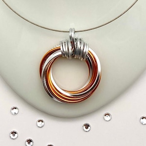 Könnte beinhalten: Eine silberne Kettenkette mit einem Anhänger aus Kupfer und Silberringen. Der Anhänger besteht aus mehreren ineinander verschlungenen Ringen.