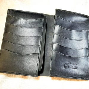 May include: A black leather wallet with multiple card slots on both sides. The interior features a debossed logo that reads Hope Leather Creations. The wallet is open, displaying a smooth, dark surface with stitched edges and curved pocket openings.