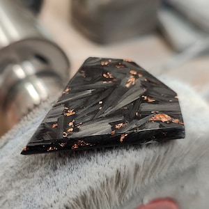 Puede incluir: Una pieza triangular de fibra de carbono negra con escamas de cobre incrustadas en la superficie.