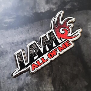 May include: A silver metal pin with a black and white "I AM ALL OF ME" text and a red and orange flame design.