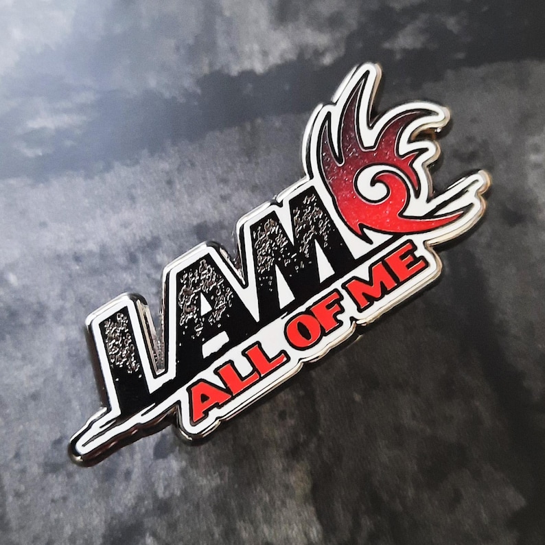 May include: A silver metal pin with a black and white "I AM ALL OF ME" text and a red and orange flame design.