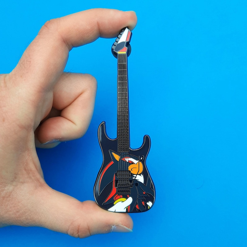 Enamel pin badge based on the ESP Shadow-II guitars, shown in hand for scale. The pins are large and measure 10cm long.