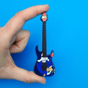 Enamel pin badge based on the ESP Sonic-II guitars, shown in hand for scale. The pins are large and measure 10cm long.