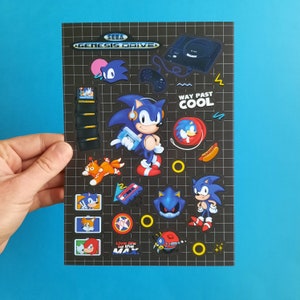 May include: A black and white sticker sheet featuring various characters from the Sega Genesis video game Sonic the Hedgehog. The sheet includes Sonic, Tails, Knuckles, and Dr. Robotnik. The sheet also includes the text "Sega Genesis Drive!" and "Way Past Cool".