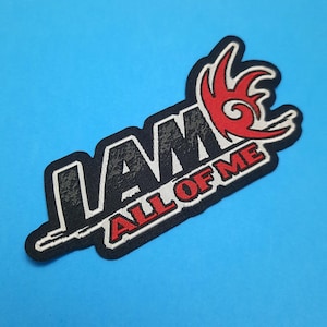 Peut inclure: Un écusson noir avec le texte "I AM" en blanc et "ALL OF ME" en rouge. Un motif graphique rouge et blanc est au-dessus du texte. L'écusson est sur un fond bleu.