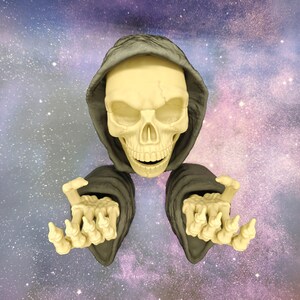 May include: A skeletal figure with a skull head and outstretched hands, wearing a gray hooded cloak. The skull is off-white with visible teeth and eye sockets. The background is a galaxy of purple, blue, and white.