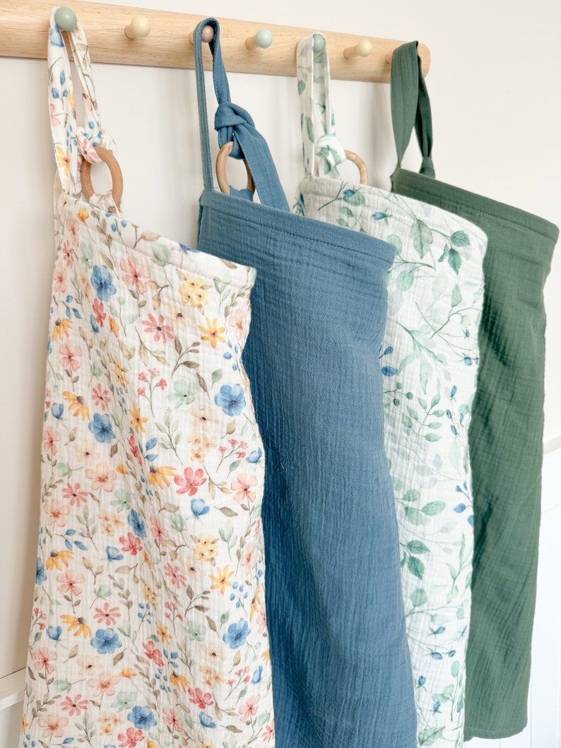 Puede incluir: Cuatro bolsas de almacenamiento de tela colgantes con diferentes patrones. Las bolsas est&aacute;n hechas de una tela suave y texturizada y tienen un anillo de madera en la parte superior. Los patrones incluyen un estampado floral, un azul s&oacute;lido, un estampado de hojas y un verde s&oacute;lido.