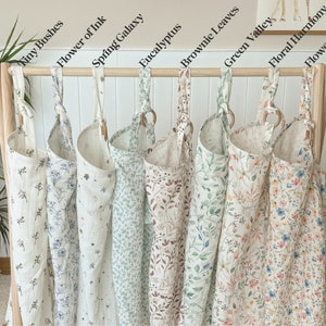 Puede incluir: Nueve bolsas de almacenamiento de tela con diferentes patrones florales colgadas de una barra de madera. Las bolsas est&aacute;n etiquetadas con nombres como "Tiny Bushes", "Flower of Ink", "Spring Galaxy", "Eucalyptus", "Brownie Leaves", "Green Valley", "Floral Harmony" y "Flower Feast".