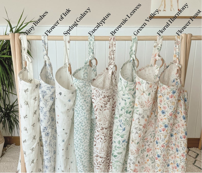 Puede incluir: Nueve bolsas de almacenamiento de tela con diferentes patrones florales colgadas de una barra de madera. Las bolsas est&aacute;n etiquetadas con nombres como "Tiny Bushes", "Flower of Ink", "Spring Galaxy", "Eucalyptus", "Brownie Leaves", "Green Valley", "Floral Harmony" y "Flower Feast".
