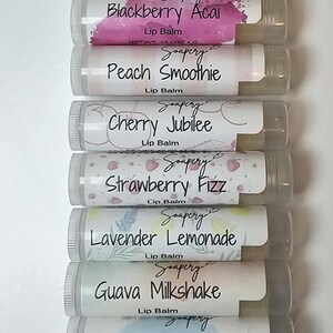 May include: A collection of twelve lip balms in clear tubes, each labeled with a different flavor name. Flavors include Mint, Spill the Tea, Pineapple, Blackberry Acai, Peach Smoothie, Cherry Jubilee, Strawberry Fizz, Lavender Lemonade, Guava Milkshake, Vanilla Mint, Simply Bare, and Watermelon Fresca.