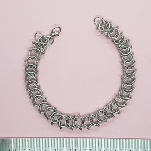 Puede incluir: Un brazalete de cadena de plata con cierre de broche. El brazalete mide aproximadamente 15 cm de largo.