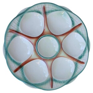 May include: A ceramic oyster serving platter in light blue and white. It features six oyster wells and a central well, with a starfish design. The rim has a lattice pattern. The platter is designed for serving oysters.
