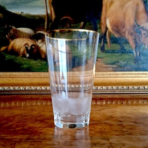 May include: A clear glass tumbler featuring a gold-toned rim and a textured diamond-cut pattern around the lower section. The glass has a straight-sided cylindrical shape with a thick, weighted base, showcasing a refined and classic design.