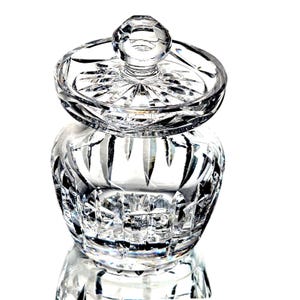 May include: A clear, cut-crystal jar with a matching lid. The jar has a rounded body and a lid with a knob on top. The crystal is intricately cut with a starburst pattern on the lid and vertical cuts on the jar's body.