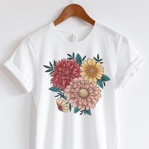 May include: White t-shirt with a floral print featuring pink, yellow, and red flowers with green leaves.