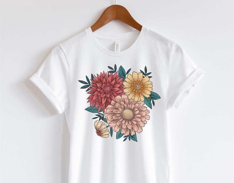 May include: White t-shirt with a floral print featuring pink, yellow, and red flowers with green leaves.