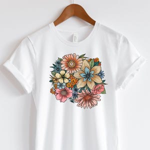 May include: White t-shirt with a colorful floral print featuring a variety of flowers in shades of pink, blue, yellow, and orange.