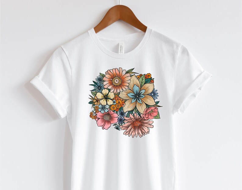 May include: White t-shirt with a colorful floral print featuring a variety of flowers in shades of pink, blue, yellow, and orange.