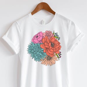 Pu&ograve; includere: Maglietta bianca con stampa floreale colorata con fiori rosa, rossi, arancioni, blu e verdi.