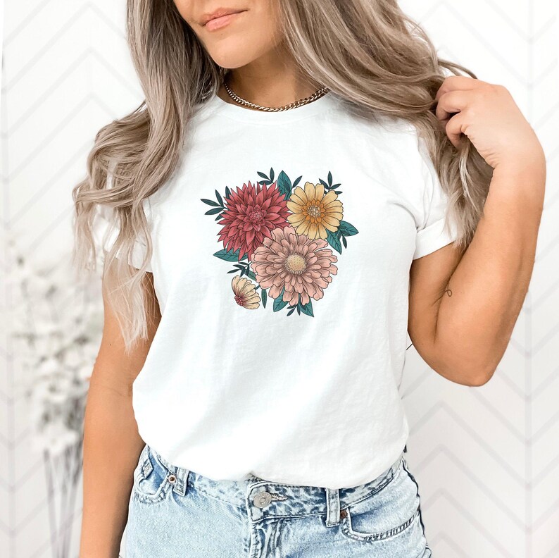 May include: White t-shirt with a floral print featuring pink, yellow, and red flowers.