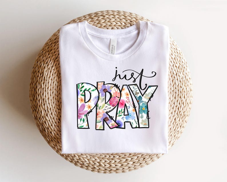 Pu&ograve; includere: Maglietta bianca con un design floreale che dice "just pray" in testo nero.