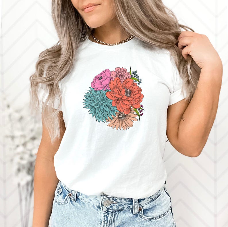 Pu&ograve; includere: Maglietta bianca con stampa di un bouquet di fiori colorati. Il bouquet comprende fiori rosa, rossi, arancioni, blu e verdi.