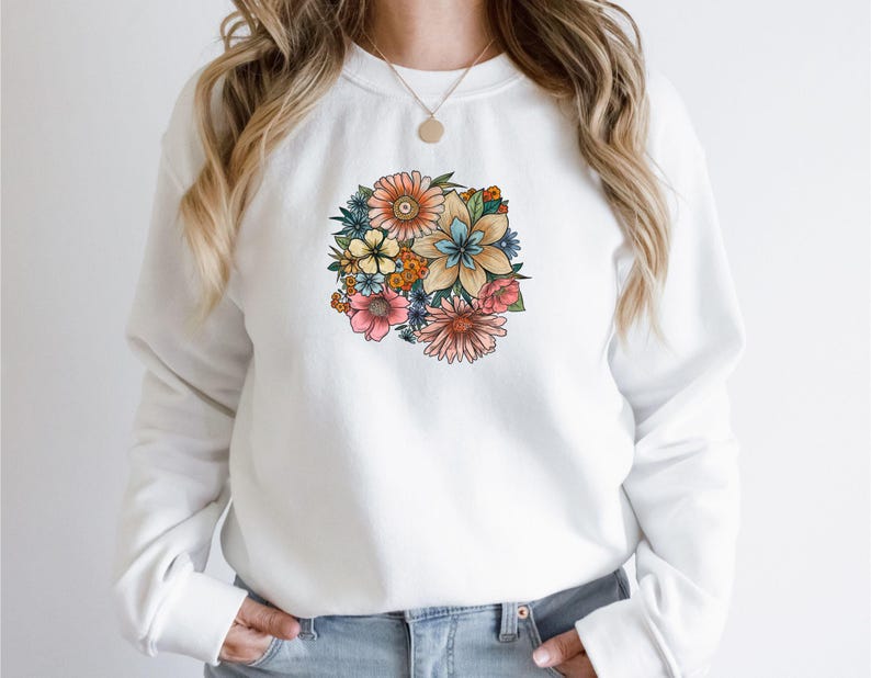 May include: White sweatshirt with a colorful floral print on the front. The flowers are in shades of pink, yellow, blue, and green.