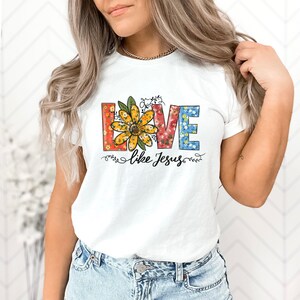 May include: White t-shirt featuring a floral design spelling out "LOVE" with a sunflower in the centre. The text "like Jesus" is below the floral design.