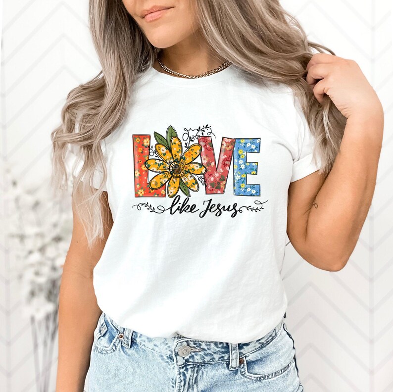 May include: White t-shirt featuring a floral design spelling out "LOVE" with a sunflower in the centre. The text "like Jesus" is below the floral design.
